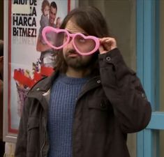 a man wearing pink sunglasses standing in front of a movie poster and holding his hands to his face