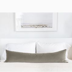 a bed with white sheets and pillows in a bedroom next to a painting on the wall