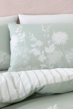 a bed with green and white pillows on it's headboard next to a pink wall