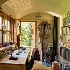 a room filled with lots of books and furniture next to a wooden table in front of a window