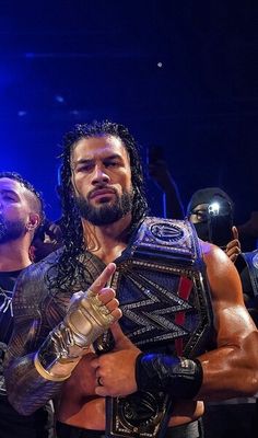 two men standing next to each other with their arms around one another and the man holding a wrestling belt