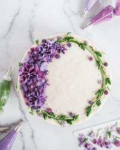 a cake decorated with purple flowers and greenery on a table next to other decorations