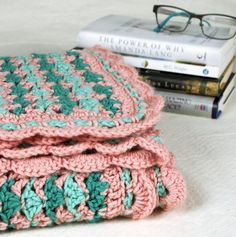 two pink and green crocheted blankets sitting on top of a bed next to a stack of books