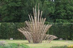 a sculpture made out of bamboo sticks in the middle of a garden with flowers and bushes