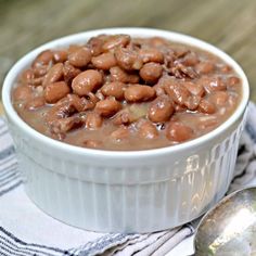 a white bowl filled with beans sitting on top of a table next to a spoon