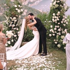 a bride and groom kissing in front of an outdoor wedding ceremony arch with white flowers