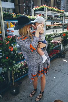 a woman holding a baby in her arms while standing next to a flower shop filled with potted plants