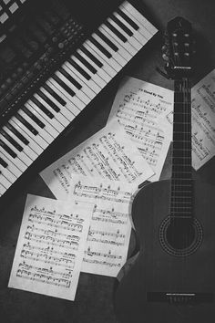 an acoustic guitar sitting next to sheet music and piano keys in black and white photo