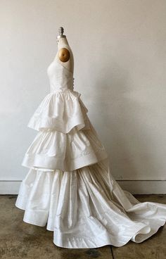 a white wedding dress is on display in front of a wall and a wooden mannequin