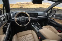 the interior of a car with tan leather seats and steering wheel, along with an open desert landscape