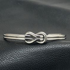 This mirror finish stainless steel round wire cuff bracelet features a simple yet stunning square infinity style love knot design. At its smallest, the bracelet can accommodate a 6 inch wrist and can go as large as you need (Great for large wrists!). The 1/4 inch band is easily adjustable by pulling or pushing together the ends. Made from stainless steel, it will NEVER tarnish and is not susceptible to scratches, dings or dents. Stainless is also hypoallergenic, making this bracelet a great alte Gents Bracelet, Wire Cuff Bracelet, Silversmithing Jewelry, Wire Cuff, Infinity Knot, Infinity Jewelry, Infinity Love, Knot Design, Jewellery Sets