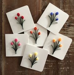 four coasters with flowers on them sitting on a wooden table, one is made out of paper and the other has buttons