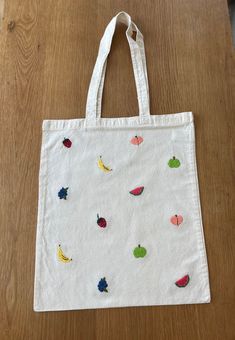 a white bag sitting on top of a wooden table next to an orange and green apple