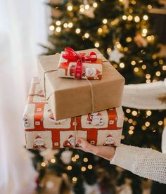 a woman holding two wrapped presents in front of a christmas tree