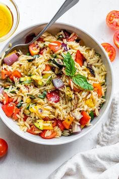 a white bowl filled with pasta salad next to tomatoes and olives on the side