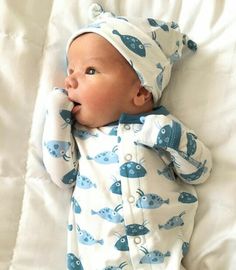 a baby laying on top of a bed wearing a blue and white fish print pajamas