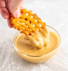 a person dipping some kind of food into a small glass bowl filled with mustard sauce