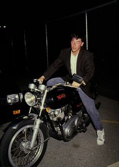 a man sitting on the back of a motorcycle at night with his hand on the handlebars