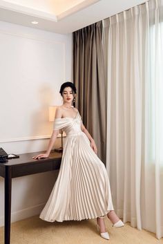 a woman in a white dress is sitting on a desk and posing for the camera