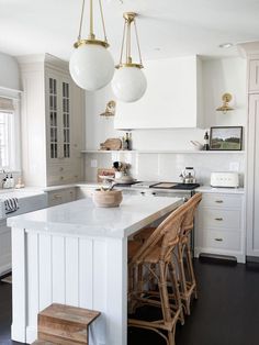 a white kitchen with wooden stools and marble counter tops, hanging lights over the island