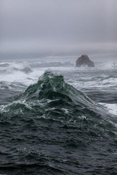 the ocean is choppy and stormy with waves crashing in front of an island that has a rock outcropping on it