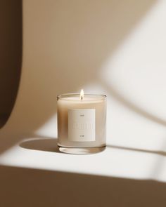 a lit candle sitting on top of a table next to a shadow from the wall