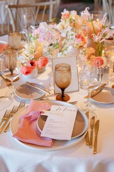 the table is set with silverware and pink napkins, gold cutlery, and flowers