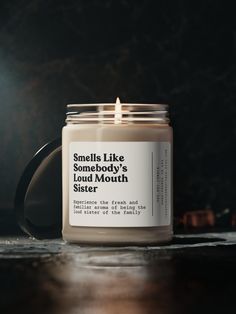 a candle sitting on top of a wooden table next to a black mug with the words smile like somebody's loud mouth sister