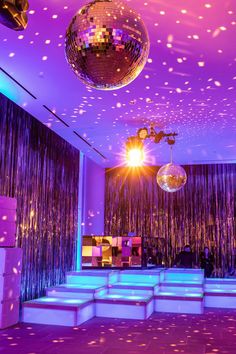 a disco ball hanging from the ceiling in front of a stage with lights and decorations