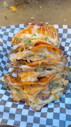 a cheesy dish is stacked on top of a checkered paper plate, ready to be eaten