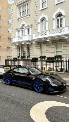 a black and blue sports car parked in front of a tall building on the street