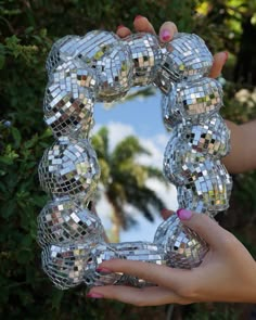 a person holding up a mirror in front of some trees and bushes with their hands