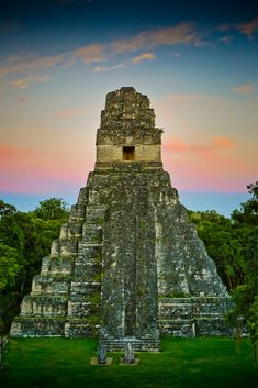 an ancient structure in the middle of a field with trees and bushes around it at sunset