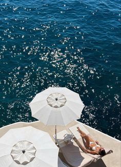 two people lounging on the back of a boat with umbrellas over their heads