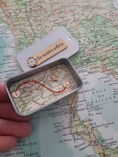 a person holding a small tin with a map in it and a tag that says no matter