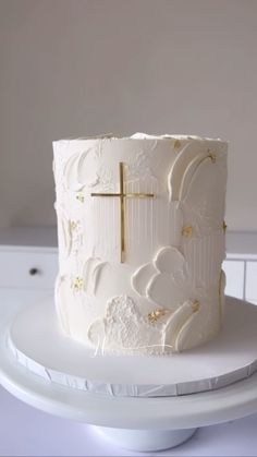 a white cake with gold decorations and a cross on the top is sitting on a plate