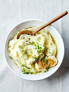 a white bowl filled with mashed potatoes and peas next to a wooden spoon on top of a table