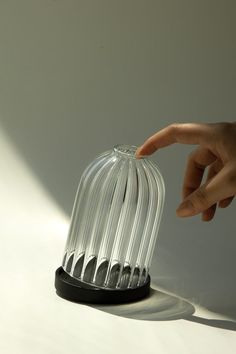 a hand reaching for an object that is shaped like a birdcage on a white surface