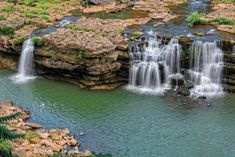 a waterfall in the middle of a river surrounded by rocks and greenery stock photos