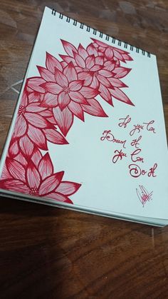 a notebook with red flowers on it sitting on top of a wooden table next to a pen