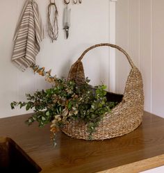 a basket that has some plants in it on a wooden table next to hooks and umbrellas