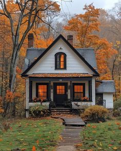 a white house in the fall with leaves on the ground and trees all around it