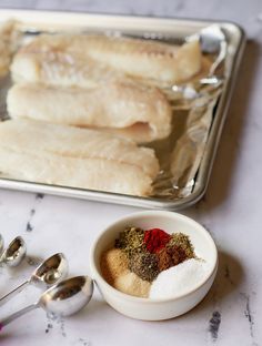 fish fillets on a baking sheet with spices and measuring spoons next to them