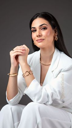 a woman in white is posing for the camera with her hands on her knees and wearing gold bracelets