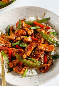 a white plate topped with chicken and veggies on top of rice next to a fork