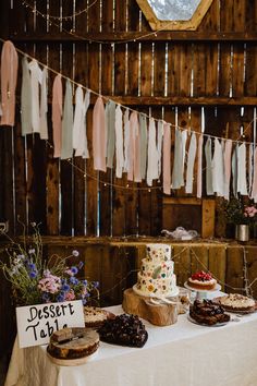 a table topped with cakes and desserts next to a wall covered in string lights