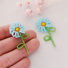 two small blue flowers are being held by someone's hand on a white surface