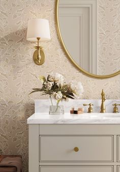 a bathroom vanity with two sinks and a large round mirror above it, in front of a wallpapered wall