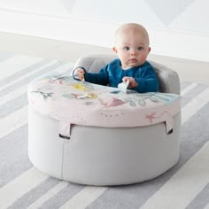 a baby sitting in a grey and pink seat on top of a carpeted floor