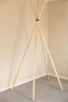 a wooden tripod stands in the corner of a room with white walls and carpet